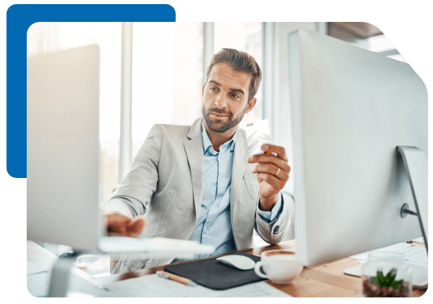 a man sits at his desk looking at his laptop while holding a payment card