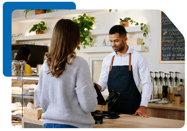 a man in a bakery shop accepting payment from a girl on his device