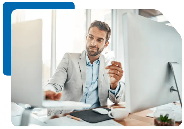 a man sits at his desk looking at his laptop while holding a payment card